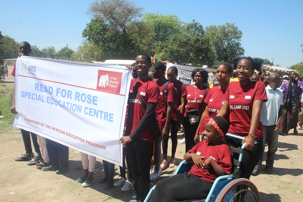 Girls and boys march behind a Read for Rose Special Education Program banner. Part of the group is a girl in a wheelchair.