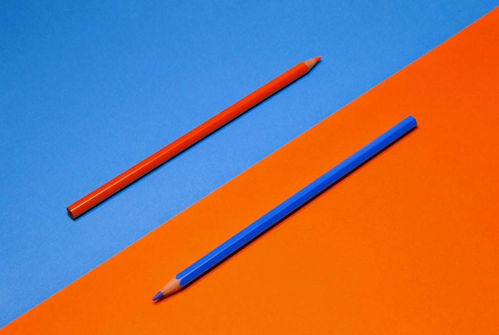 Rectangular image split in half diagonally. One half has a blue background with an orange pencil on top, the other has an orange background with a blue pencil on top.