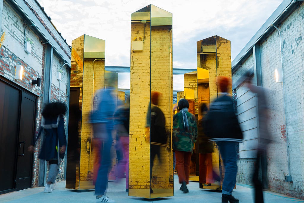 Menschen laufen durch eine gelb-spiegelnde Installation.