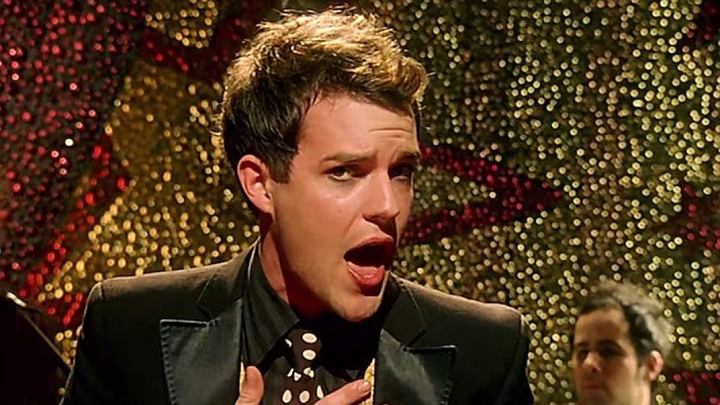 A man dressed in a black suit singing against a sparkly gold and red backdrop