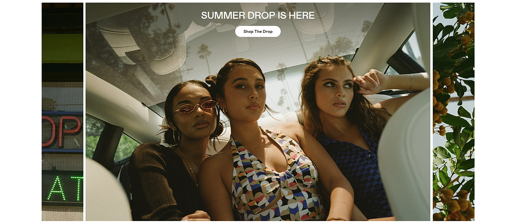 A hero section in the Social Tourist website marketing the summer collection, consisting of a bespoke photograph of three girls in a car wearing the clothes, a big title and a call to action button.
