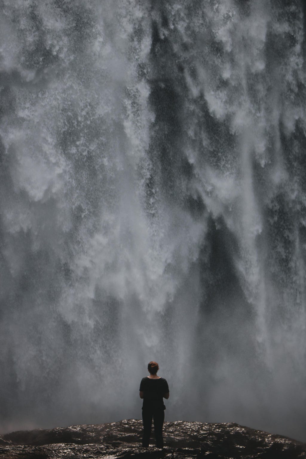 Woman standing in front of massive waterfall.