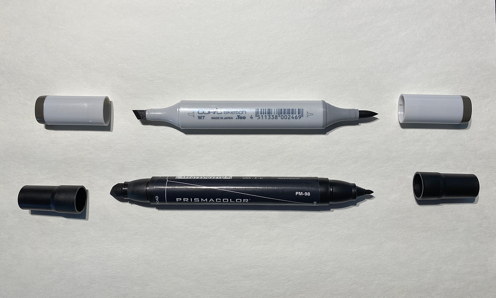 A gray Copic marker above a black Prismacolor marker, both with the lids off of both ends