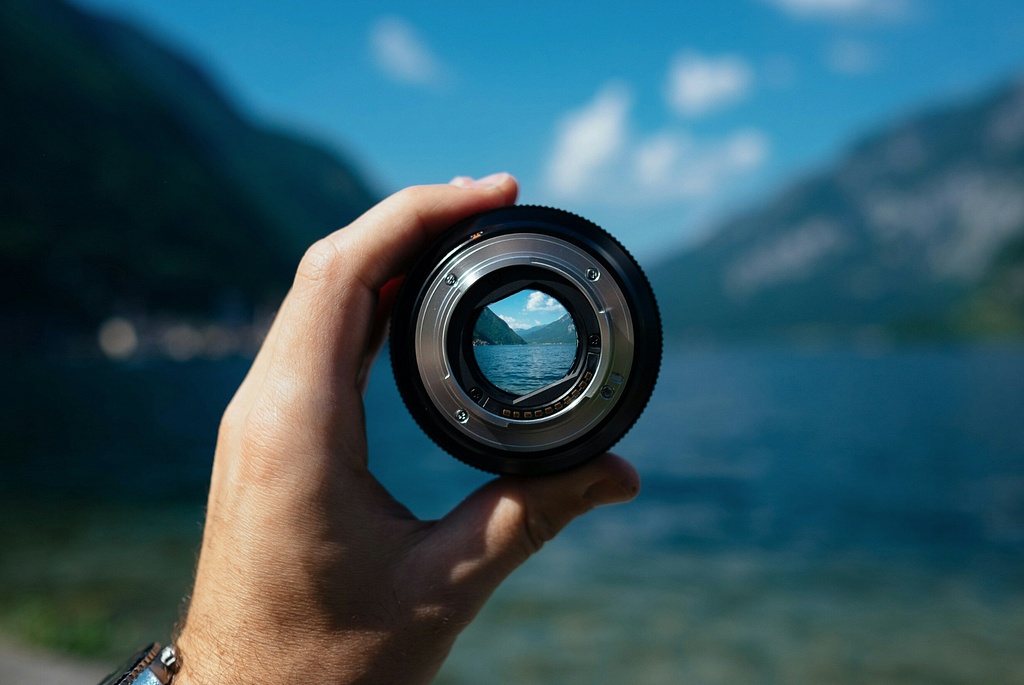 A hand holds a camera lens in front of a landscape