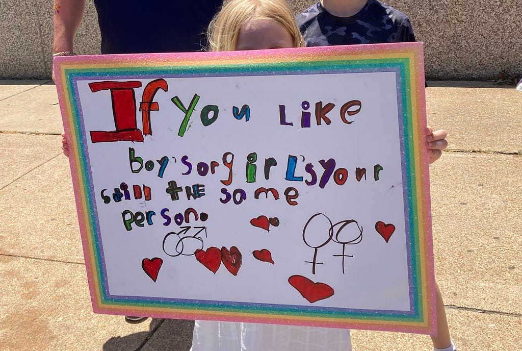 Close up of father, son, and daughter together at Pride parade in St. Louis. The young girl holds up a handmade colorful sign saying “If you like boys or girls your [sic] still the same person.”