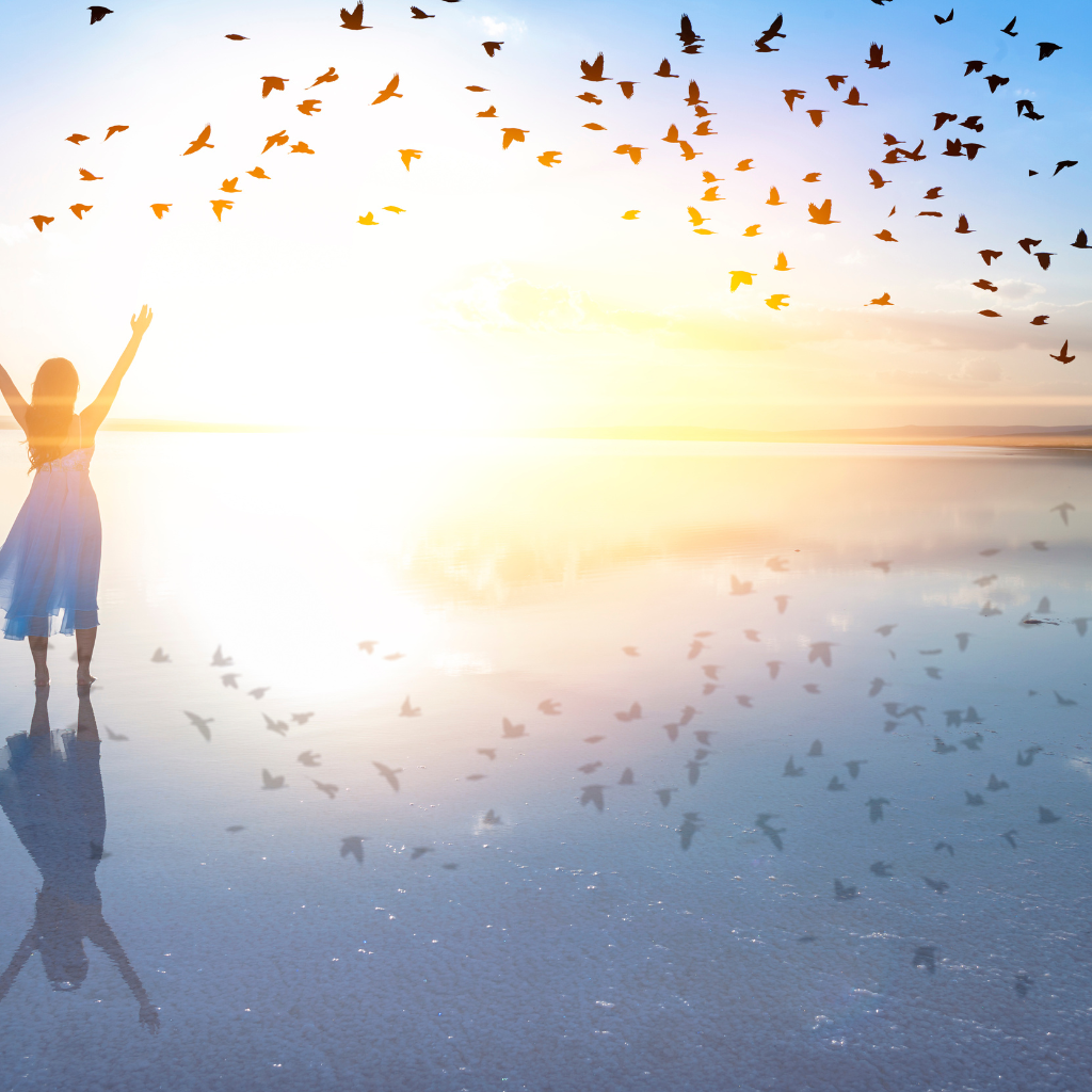 Woman with raised hands near the ocean, birds flying above, representing freedom and growth