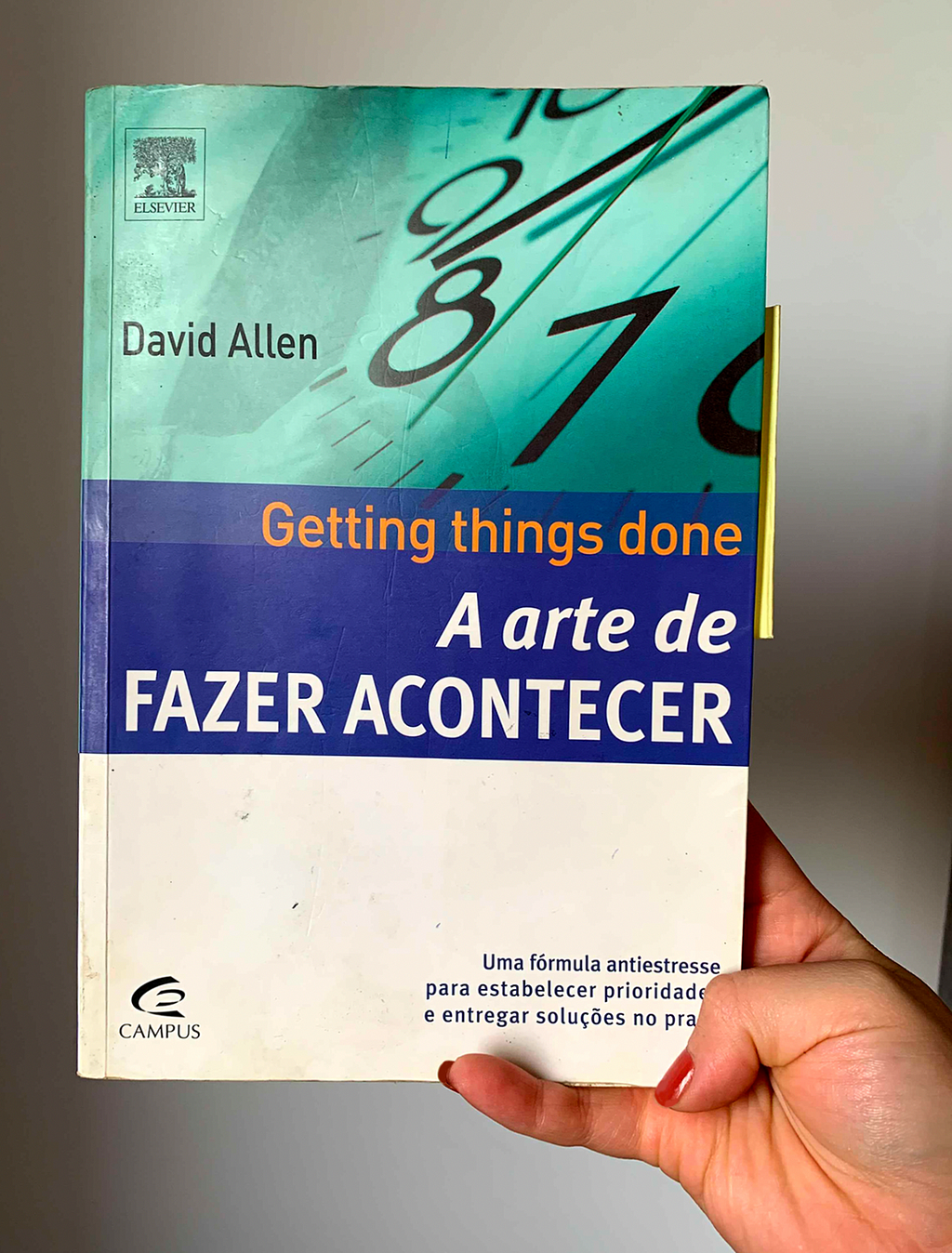 Foto de um livro verde, azul e branco. Na capa no topo superior esquerdo está o nome do autor: David Allen. Ao centro se encontra os dizeres: "getting things done — a arte de fazer acontecer"