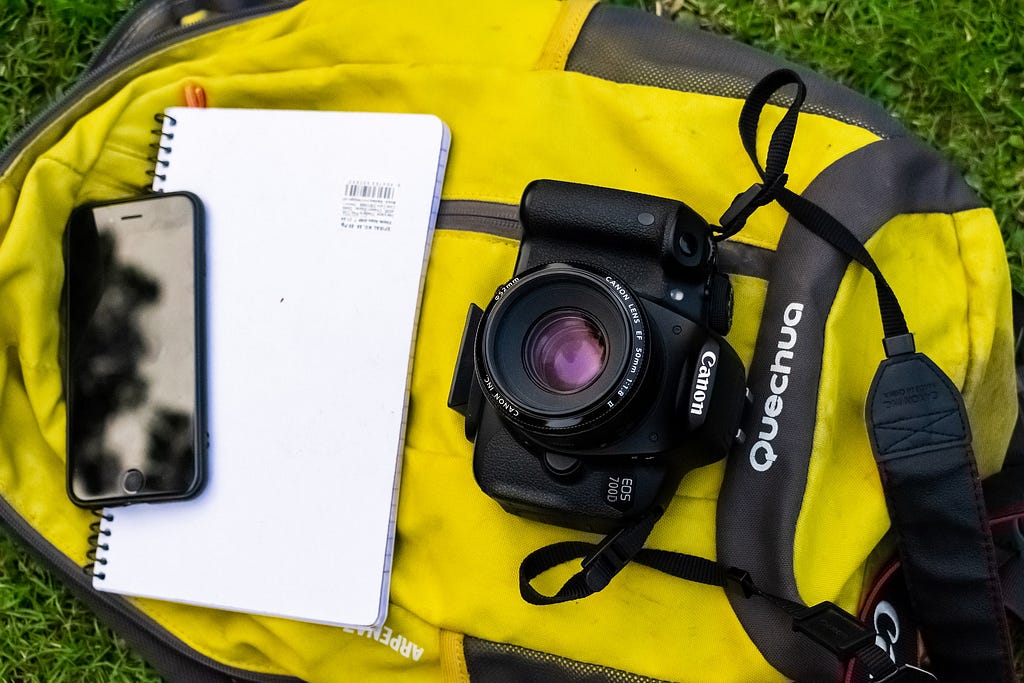 photo of cell phone, DSLR canon camera, note pad, set upon a yellow bag