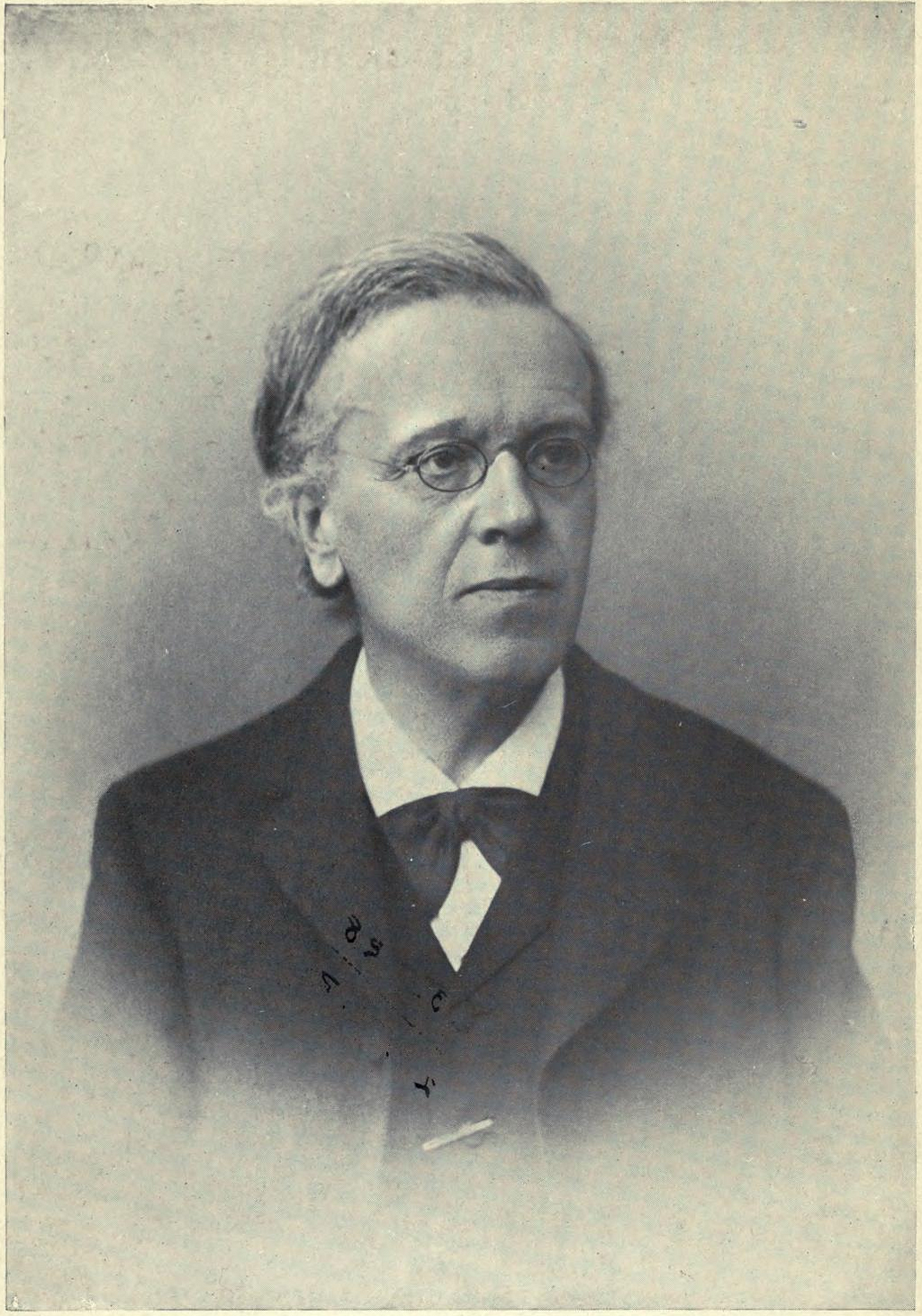 Black and white photograph of Franz Overbeck, in a suit, wearing thing rimmed glasses. Photo by August Höflinger.