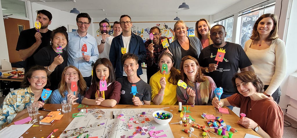 A group of 18 designers holding handmade paper lollies during a creative crafting activity at an offsite team day