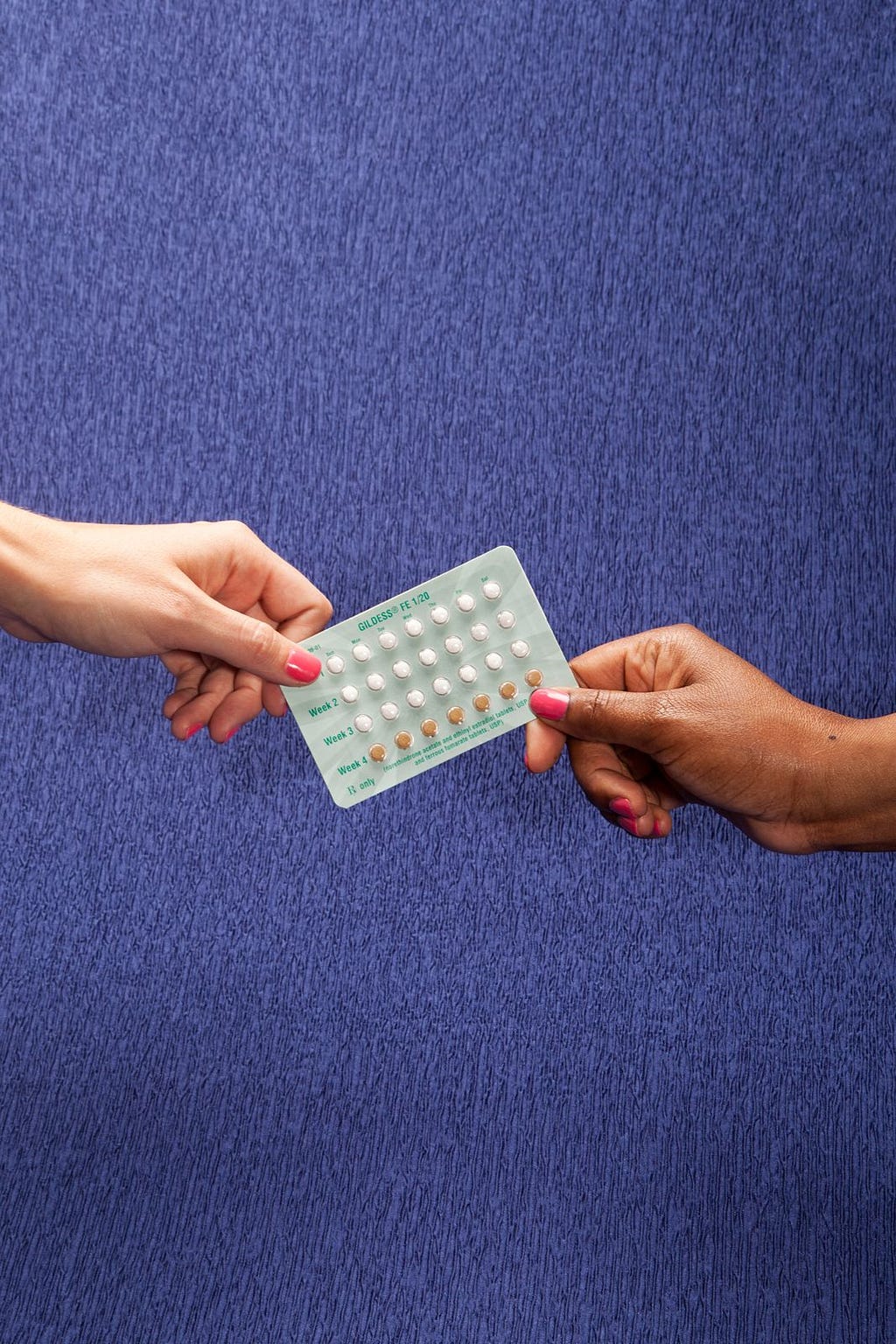 Two hands holding a pack of brown and white contraceptive pills