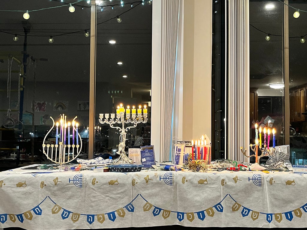 A table decorated for Hannukah in front of a window with 4 menoras lit with 5 candles and a shamash each