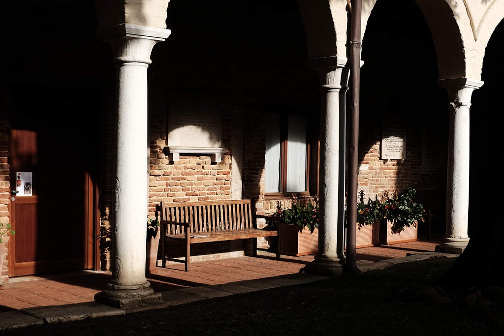 contrast-y image of a bench in the sun with bright columns in front of a shadowed background