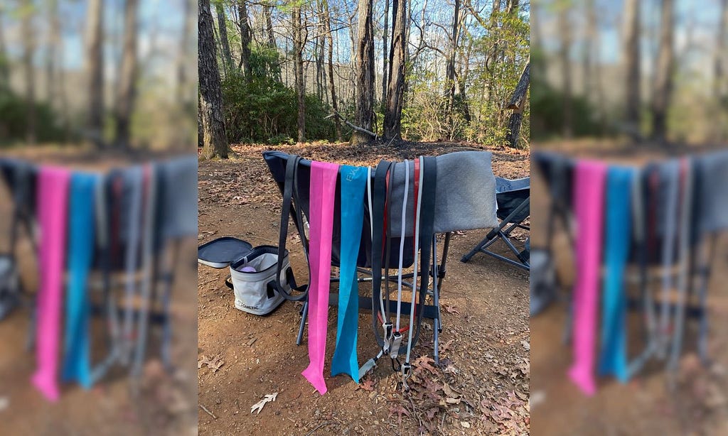 A collection of resistance bands hung over a camp chair at a campsite in the forest