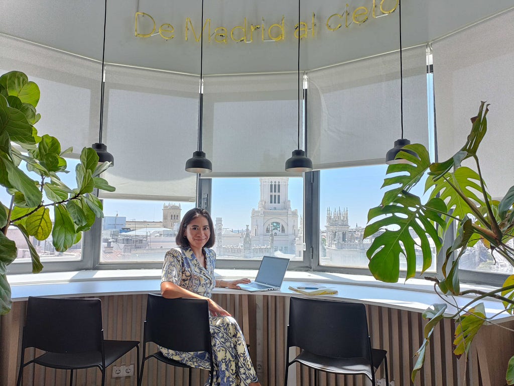 a female sitting in a desk, working close to a window with view over Madrid