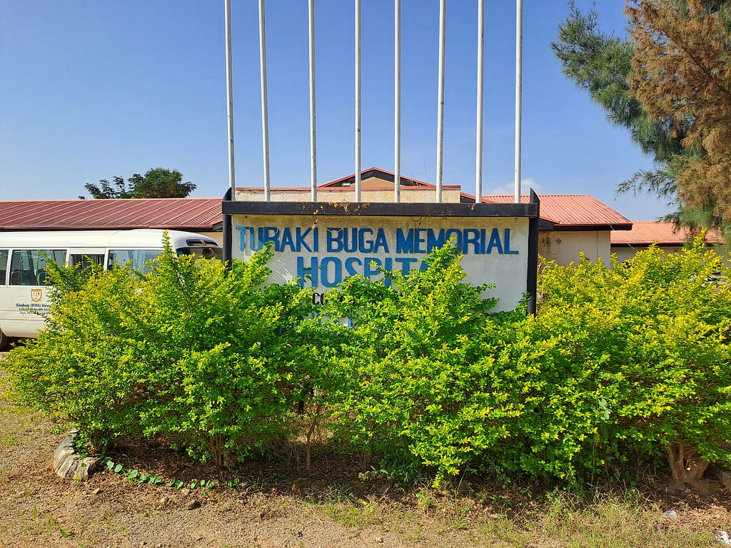 A signpost depicting Turaki Buga Memorial Hospital. The school bus is parked just behind it.