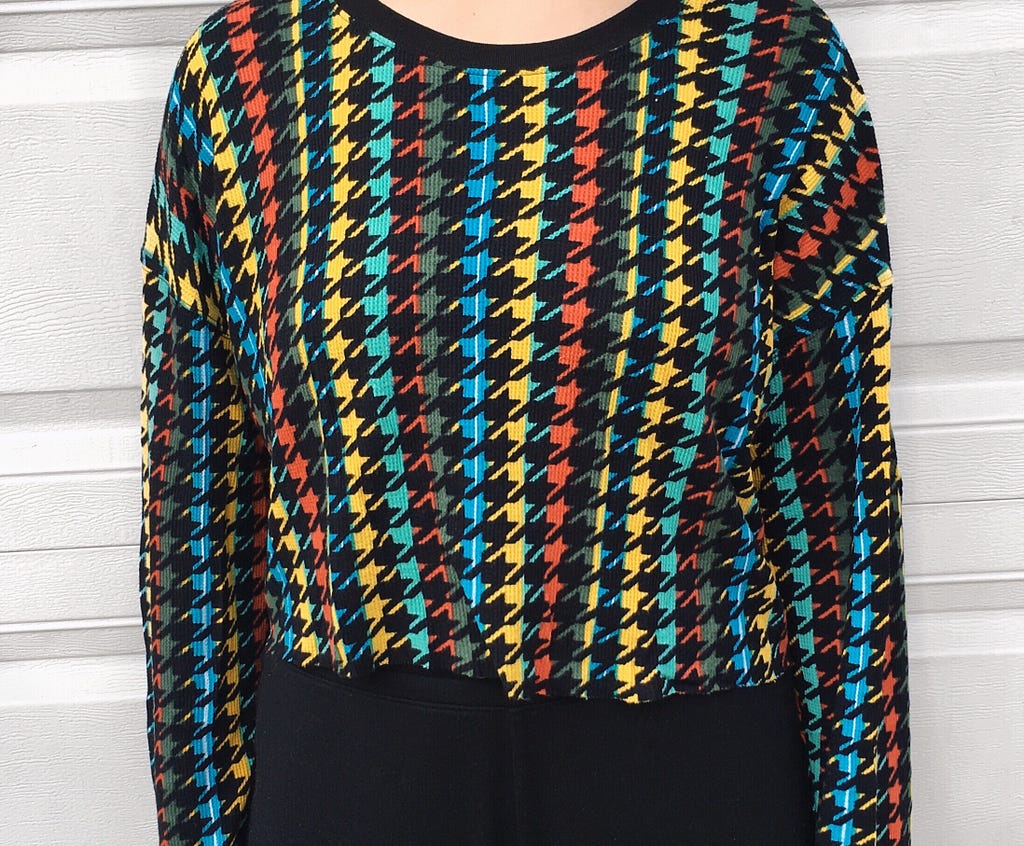 A blue, green, yellow, red, and black patterned retro sweater worn with black joggers.