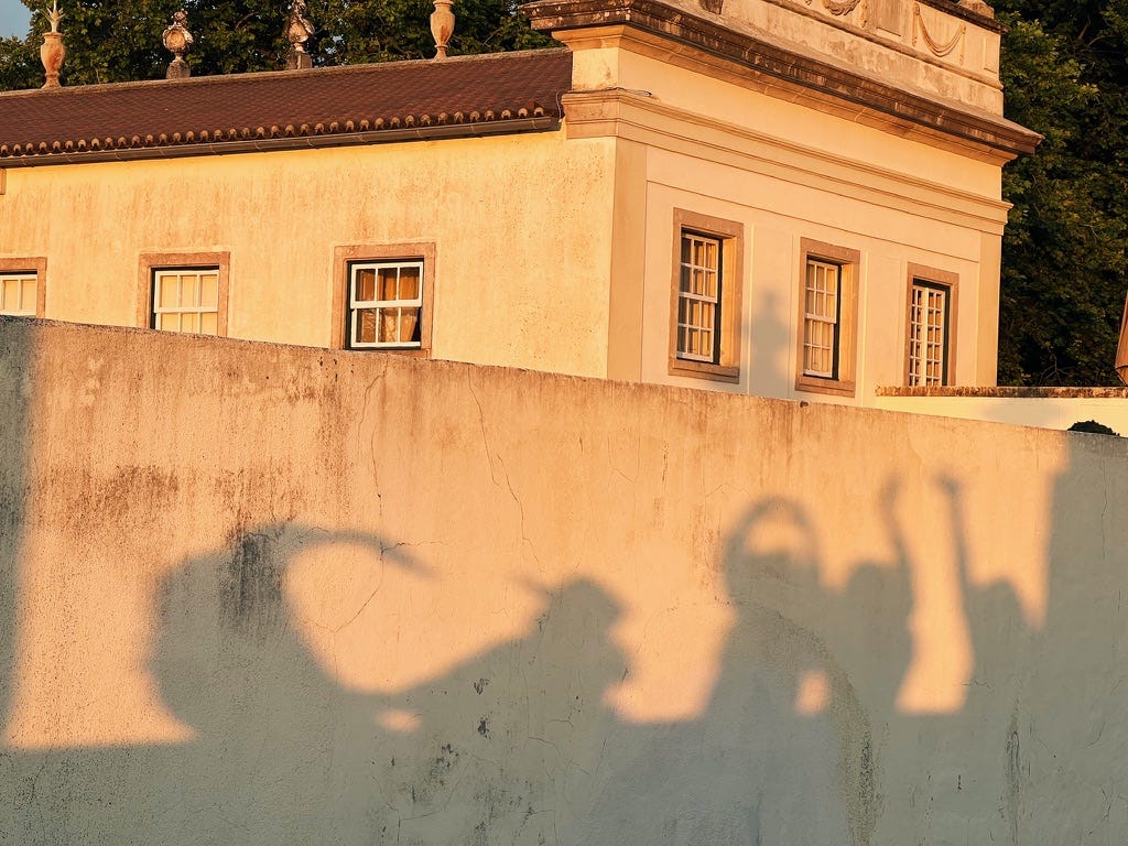 An orange sunset reflects on the walls of old Portuguese buildings, with friends creating shadows with the glow of the light. Sintra, Portugal.