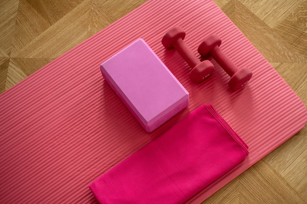 Pink yoga mat on parquet floor with pink block and pick towel
