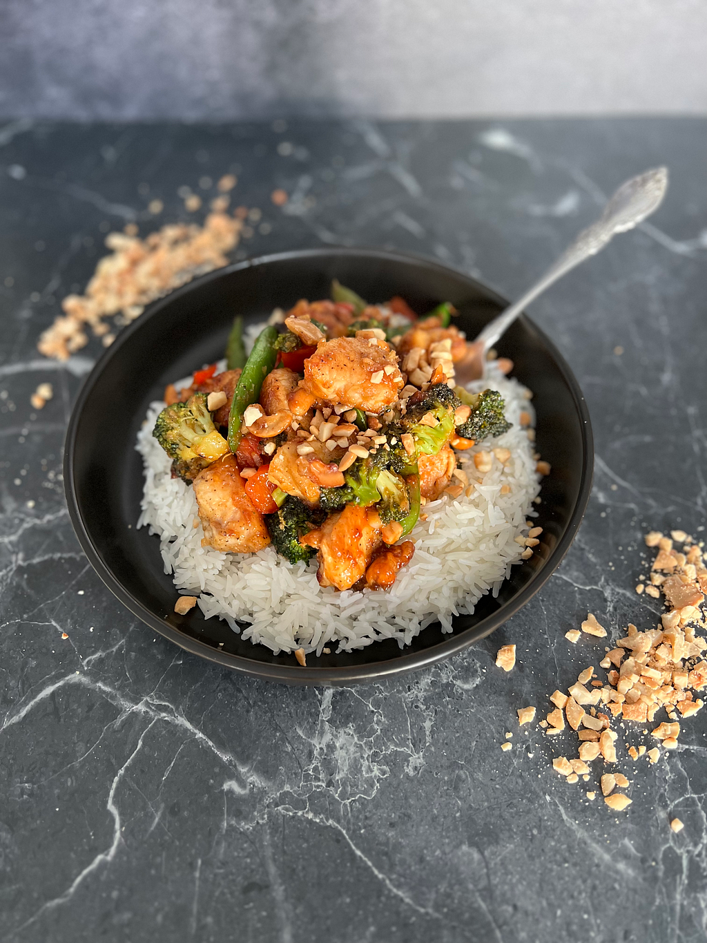 Cashew chicken stir fry on a marble surface with crushed peanuts