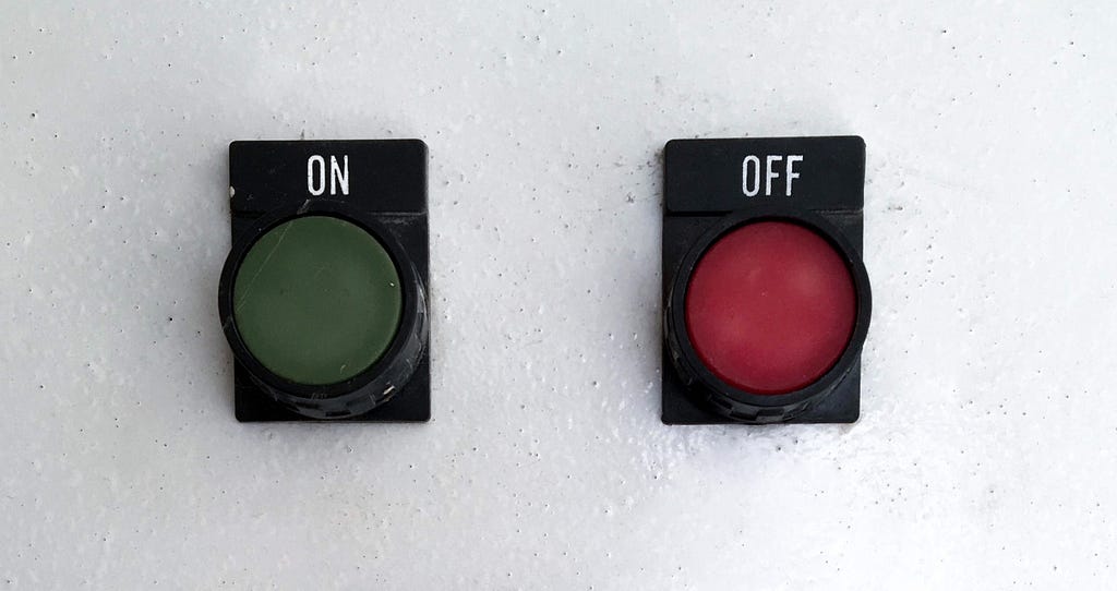 A dark green button marked ‘ON’ and a dark red button marked ‘OFF’ on a white wall. The ‘OFF’ button is pressed.