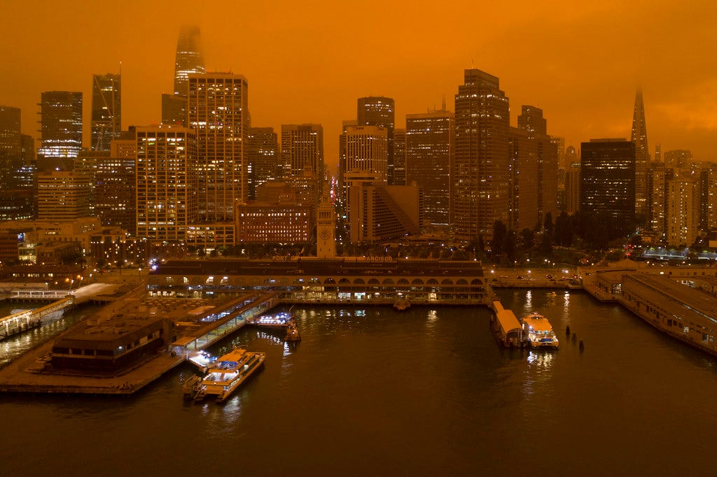 Photograph of a waterfront with tall buildings. The sky is hazy and orange with smoke.