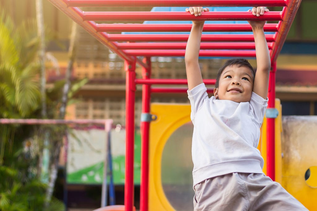 Happy student​ playing and hanging from a steel bar at the playground