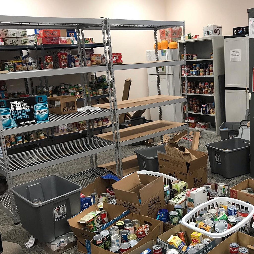 Two large empty shelves sit behind stacks of donated food in boxes and baskets