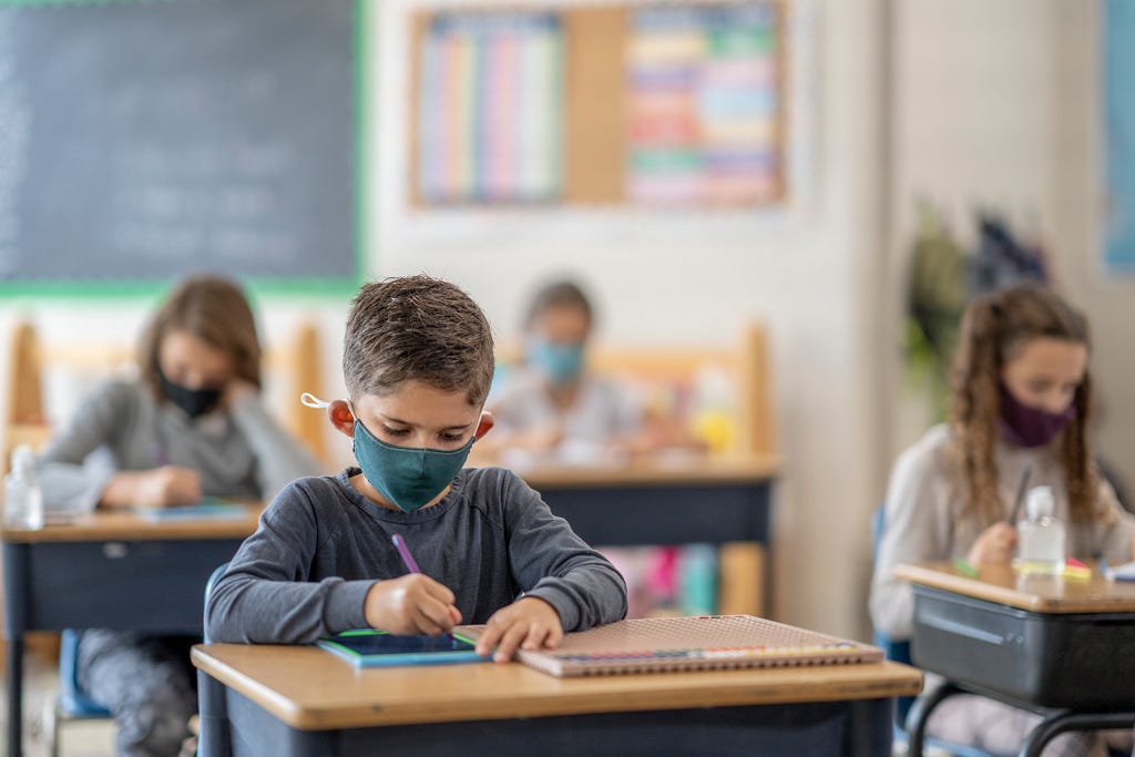 A student wearing a mask works at a school desk.