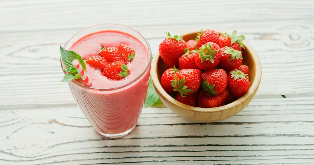 Fruit smoothie with some strawberries on top and a bowl of strawberries