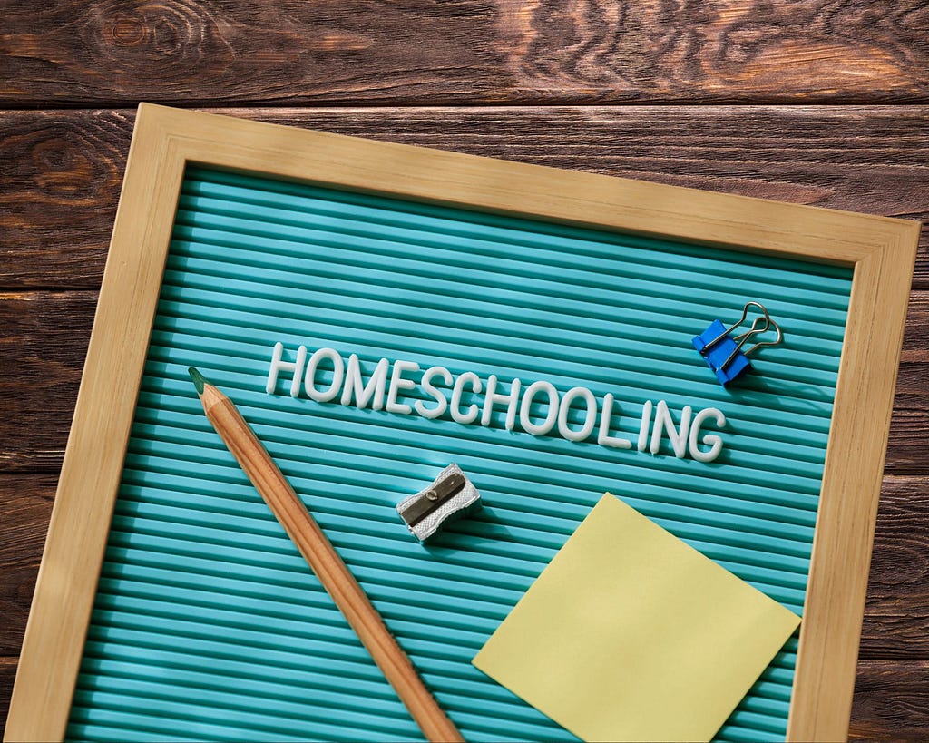 A board where homeschooling is written. There is a pencil, a pencil sharpener, a paper clip, and a sticky note on the board.