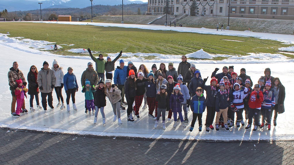 Photo of several World Ice Skating Day participants standing on the outdoor Olympic Speed Skating Oval and smiling.