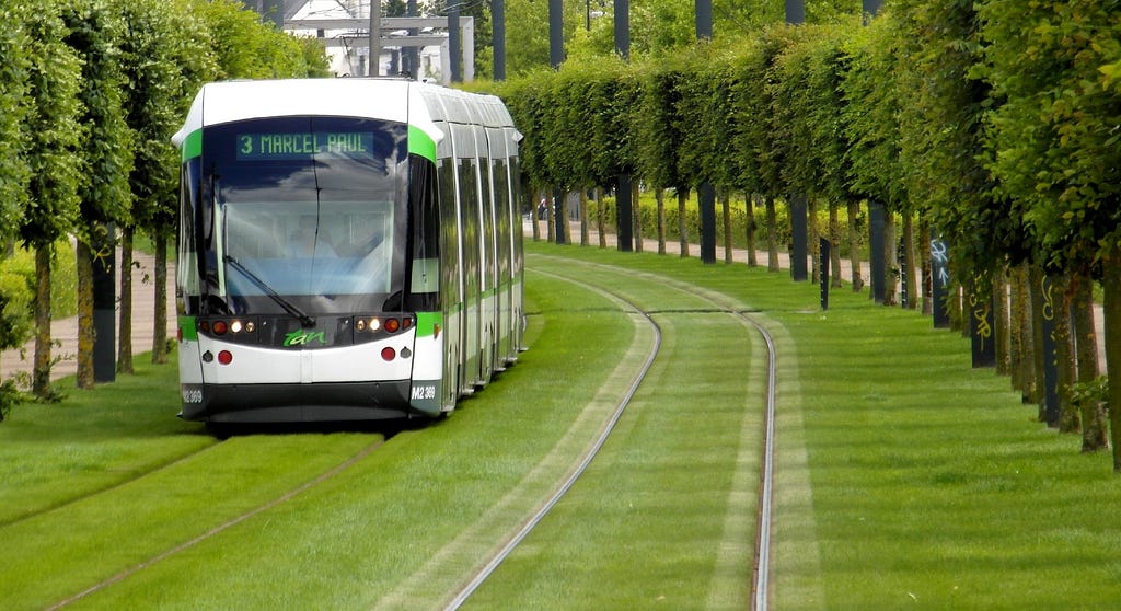 A tram travelling on a set of tracks, surrounded by grass and trees that form a beautiful green corridor through Nantes, France