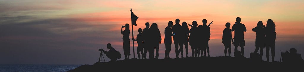 A group of people contemplating the Tanah Lot Temple in Indonesia with a sunset background