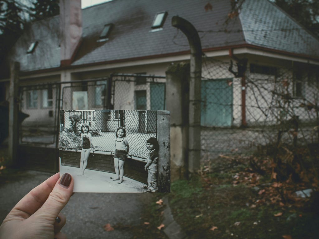 A photo of an old house superimposed in front with a old black and white photo of three children at the same building years ago. Photo by Anita Jankovic on Unsplash