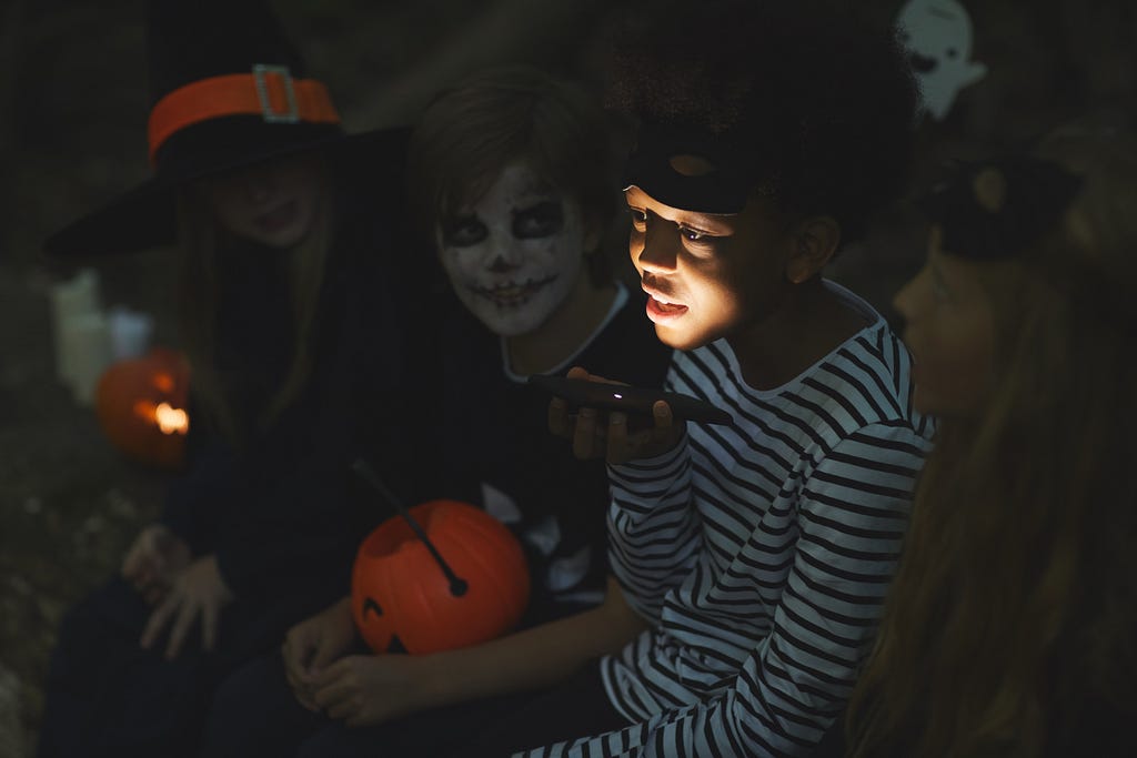 Group of kids telling scary stories on Halloween. Young boy telling the story is holding a torch underneath his chin.