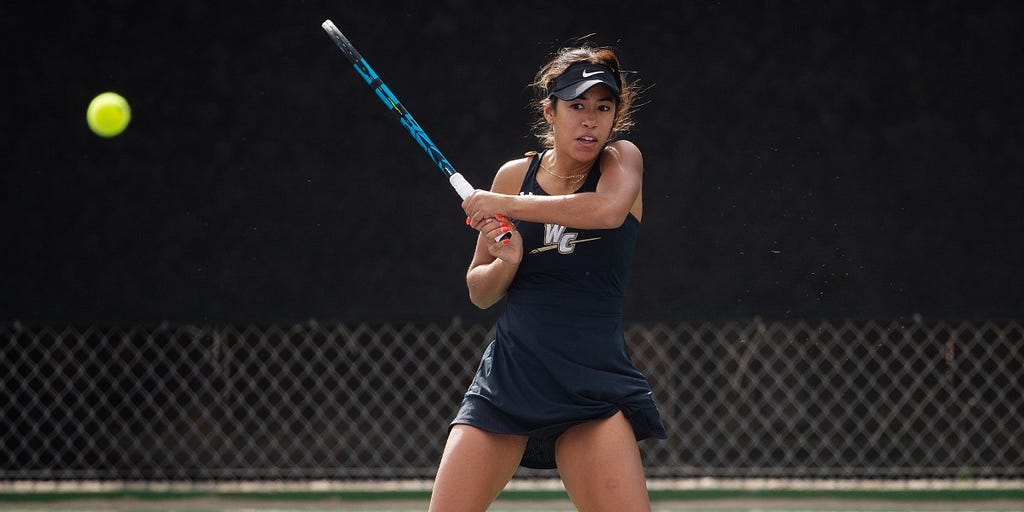 Action shot of a Whittier College Women’s Tennis player playing tennis. She is on the court with her blue racket and black Tennis ensamble.
