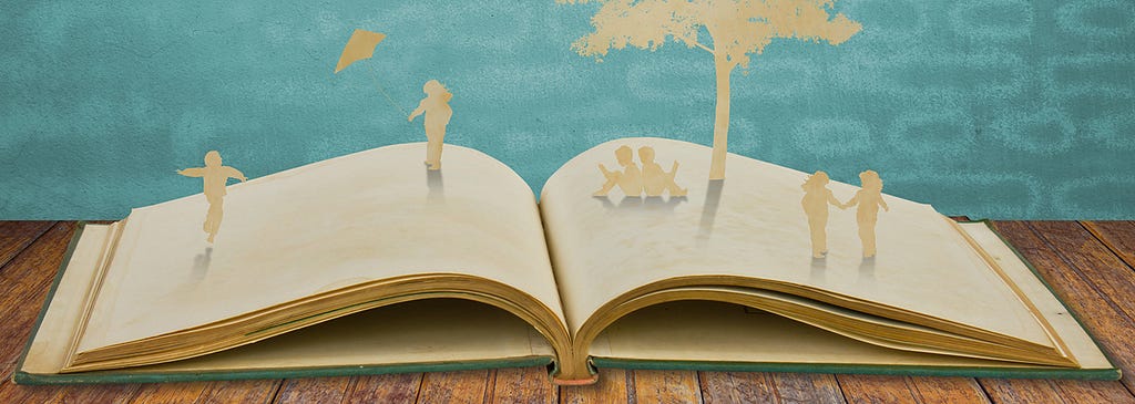 book opened on wooden table. emerging from book are beige silhouette of young children sitting reading a book under a tree