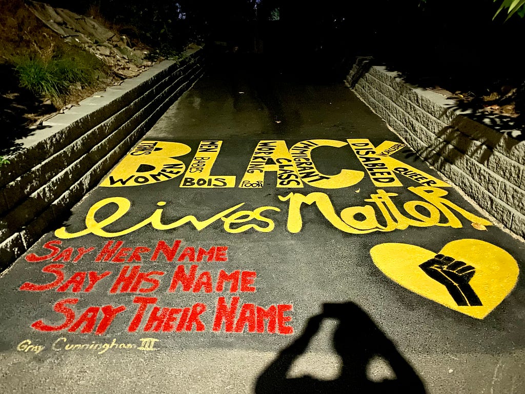 Photo of an artwork drawn on a driveway that reads “Black Lives Matter. Say Her Name. Say His Name. Say Their Name.”