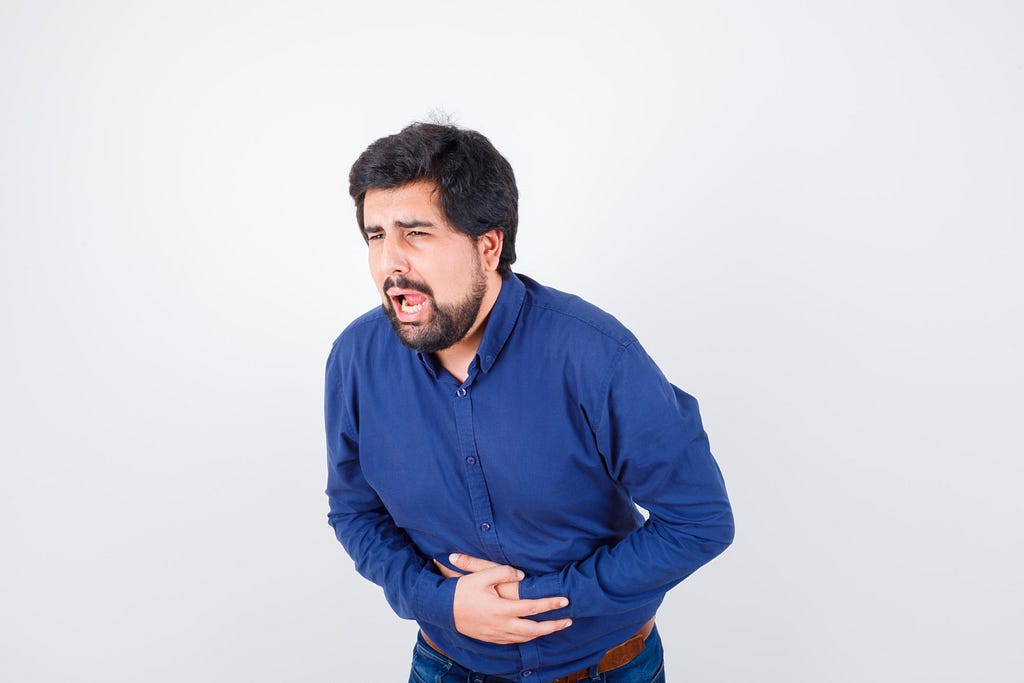 young male in blue shirt suffering from stomach ache due to cholecystitis