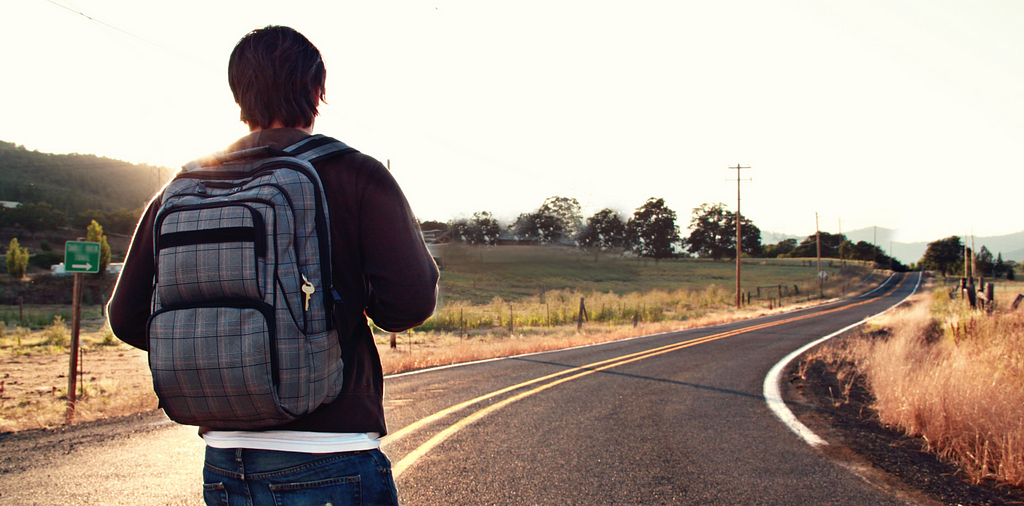 Stock photo of a man with a backpack standing on a long, winding road in the countryside