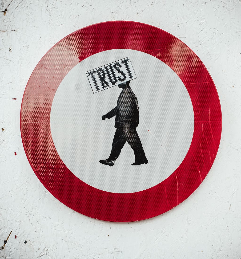 a red circle with a silhouetted figure of a person where the image of the head is blocked by a sign of the word “Trust”