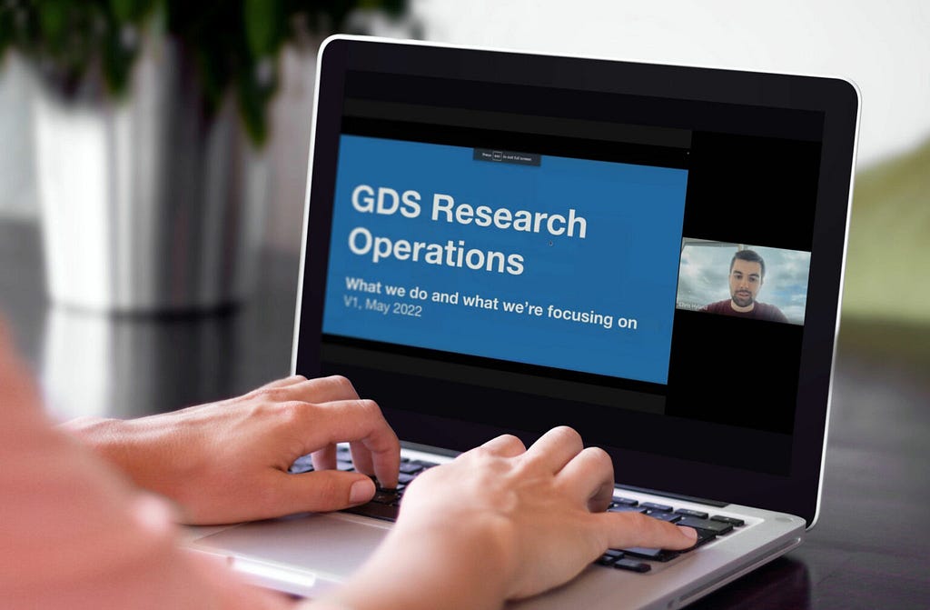 Hands on the keys of a silver laptop with a slide that says GDS Research Operations.
