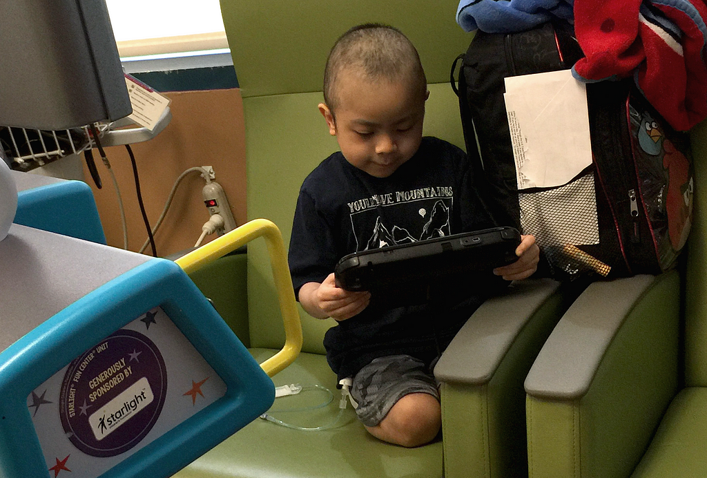 Starlight Kid Andrew plays on a Starlight Gaming station while sitting in a chair.