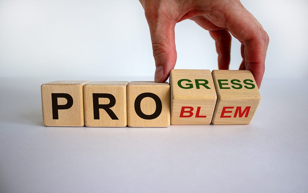 Hand flips cubes with letters on them and changes the word ‘problem’ to ‘progress’