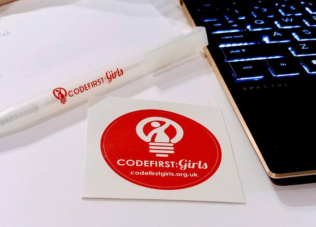 A CodeFirst:Girls sticker and pen with a laptop in the background.