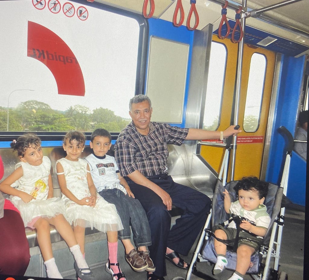 A man sits on a train car with four children, one of them in a stroller.