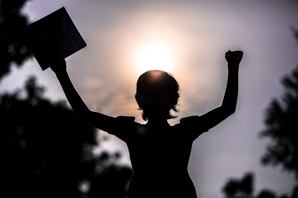 Sihouette of a girl holding a book against the backdrop of a sunny sky