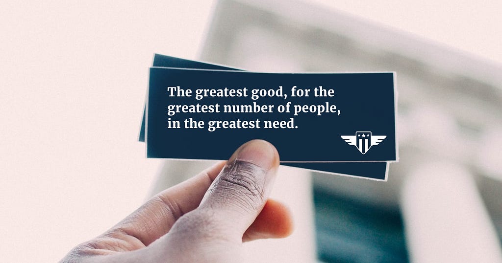 A brown thumb and index finger holding small cards that read: The greatest good, for the greatest number of people, in the greatest need.