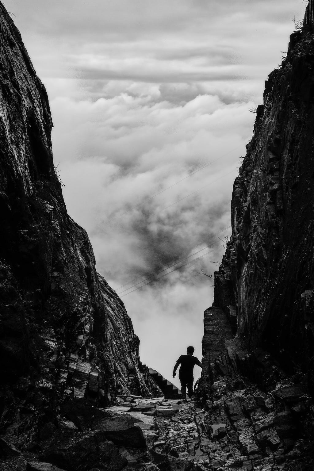 Black and white image of a mountain pass with a runner in between two rock faces and lots of white cloud